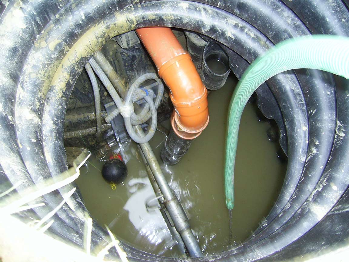 How Getting Rid Of Septic Tank Sludge Aids In Preventing Groundwater Contamination 1 Inside view of a septic tank with sludge, orange pipes, and green hose for wastewater management.