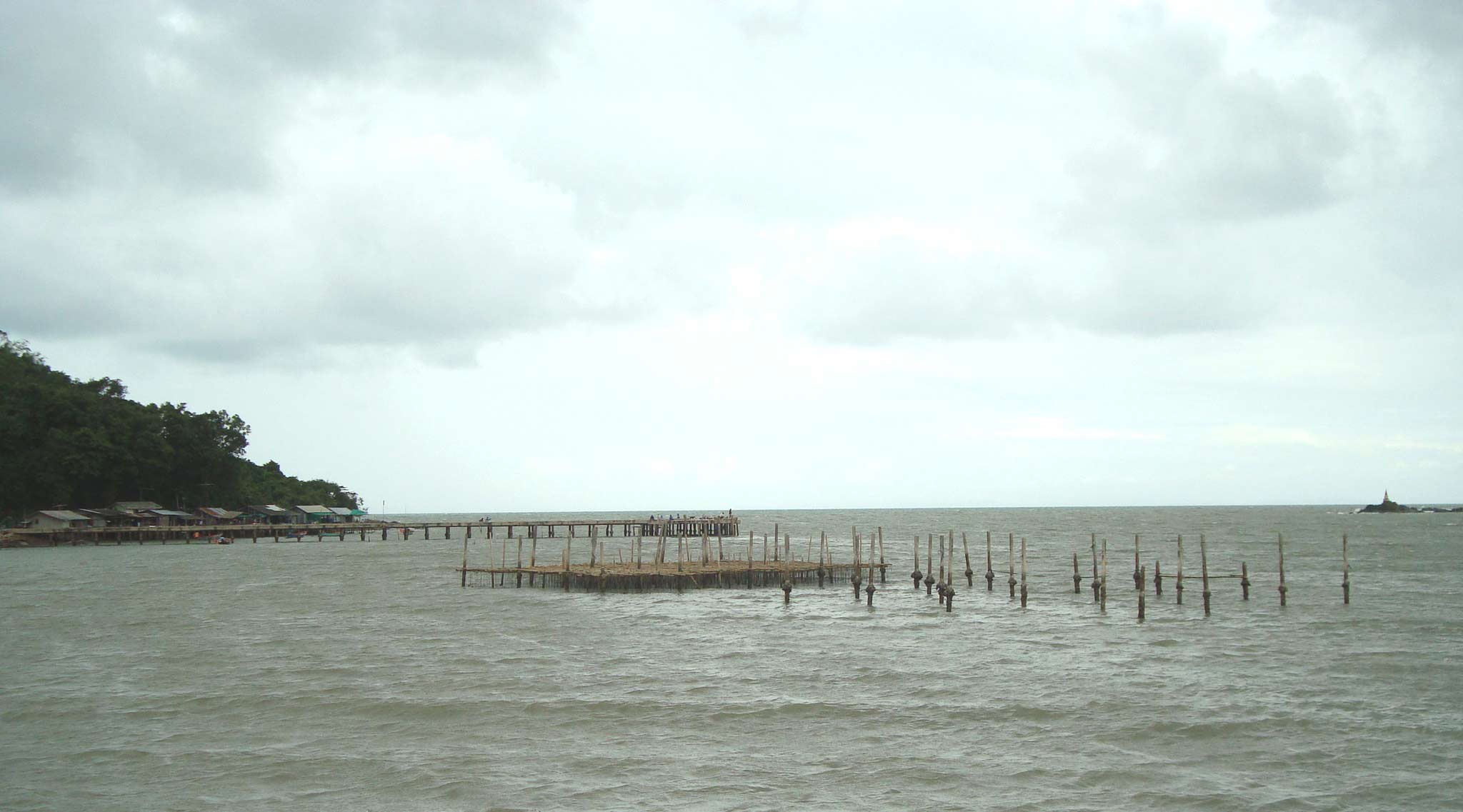 How Biofloc Fish Farming Can Boost Aquaculture in Myanmar 1 A traditional coastal aquaculture site with a pier and wooden posts in murky water, representing the challenges that require sustainable solutions like biofloc technology.