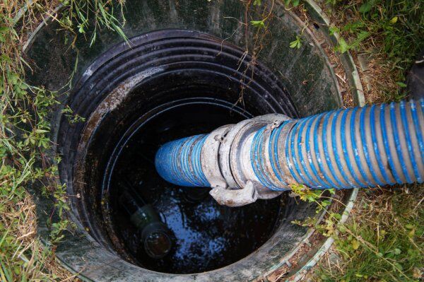 How Additives Help In Maintaining Good Septic Tank Health 1 Blue hose in a septic tank, applying additives to treat waste in a grassy area.