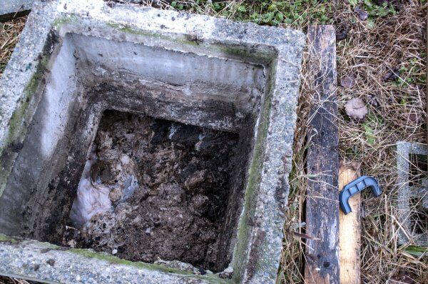 What Are The Objectives Of Faecal Sludge And Septage Treatment? 1 An open, square concrete septic tank showing faecal sludge and septage, highlighting the need for treatment.