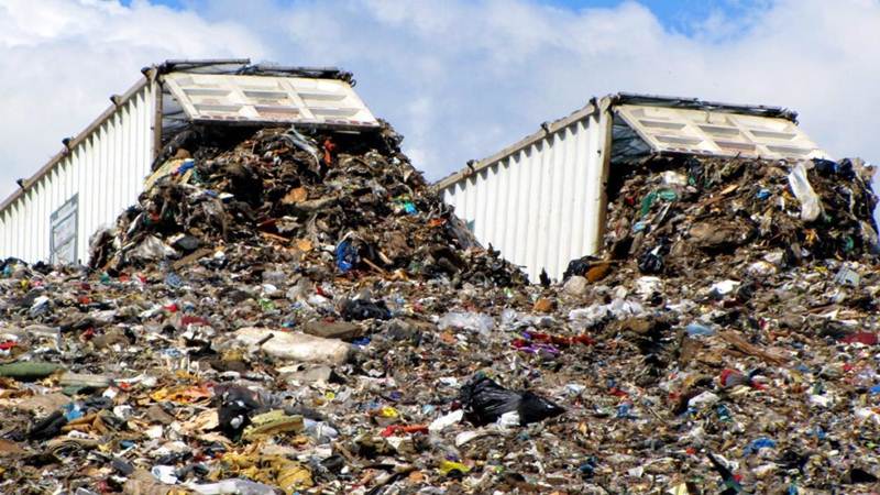 The Future of Solid Waste Disposal and Management 1 Large pile of mixed waste at a landfill with two overflowing containers under a partly cloudy sky.