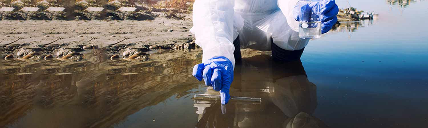 How Usage of Chemicals Affect Natural Enzymes in Septic Tank 1 A person in a hazmat suit and blue gloves takes water samples from a murky natural body, symbolizing chemical impact on natural enzymes in septic tanks.