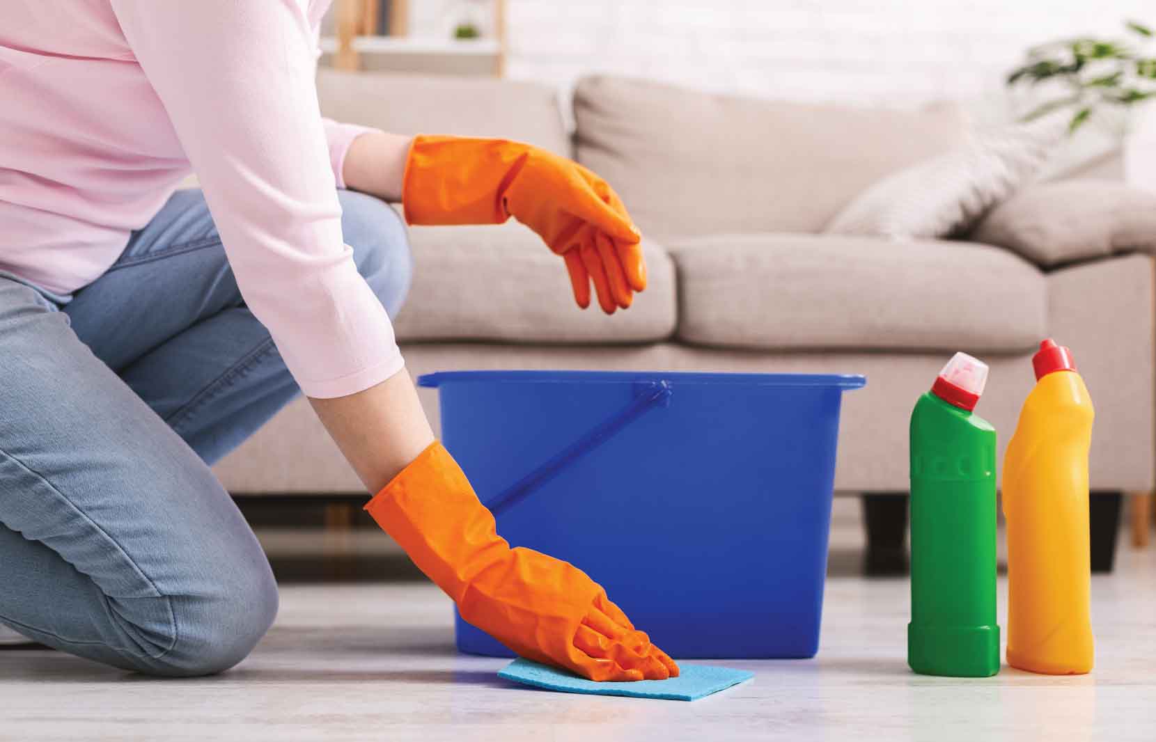 Cleaning Agents and How They Impact Indoor Air Quality 1 Person in orange gloves wiping floor with a cloth, next to a bucket and cleaning bottles, representing cleaning agents' impact on indoor air quality.