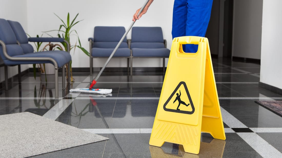 Green Cleaning: Understanding Bio-enzymatic Cleaners & Its Benefits 1 Person mopping floor in office with caution sign, showcasing bio-enzymatic cleaner use for safe cleaning.