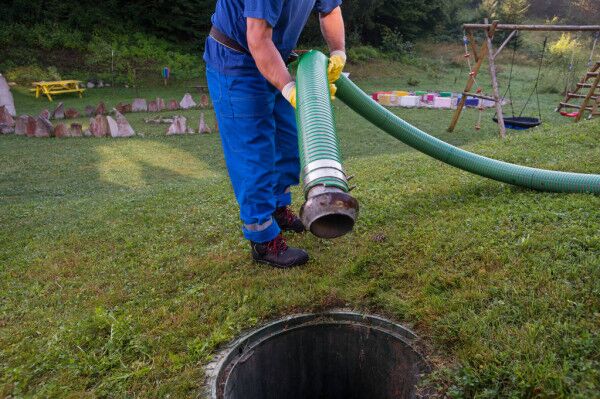 How Can Septic Tank Cleaner Help Sewage Workers In Kenya 1 A worker in gloves lowers a hose into an open septic tank in a grassy area, demonstrating septic cleaning in Kenya with emphasis on safety.