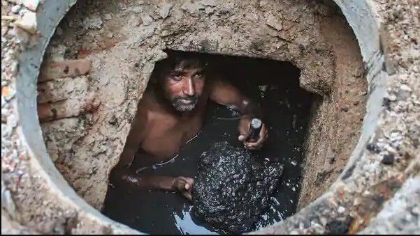 Septic Tanks: How We Can Stop Them From Turning Into Lethal Gas Chambers 1 A man immersed in raw sewage inside a manhole, performing manual scavenging, highlighting hazardous labor.