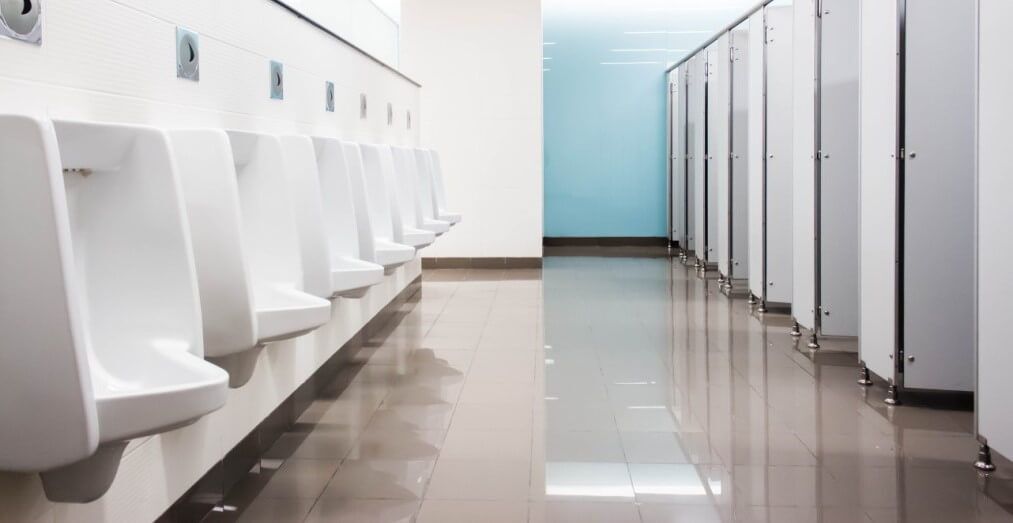 Sources of Washroom Odor in Corporate Offices & How to Eliminate It 1 Clean public restroom with urinals and stalls, highlighting common washroom odor sources like urine and bacteria buildup.