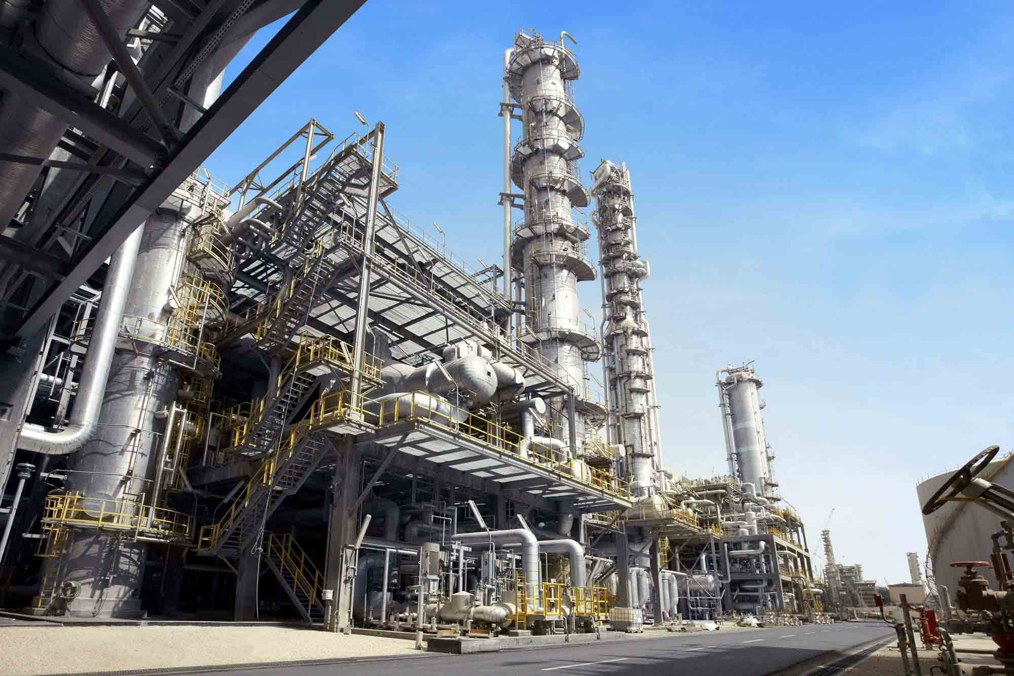 Petrochemical plant with tall towers, pipes, and steel structures under a clear sky.