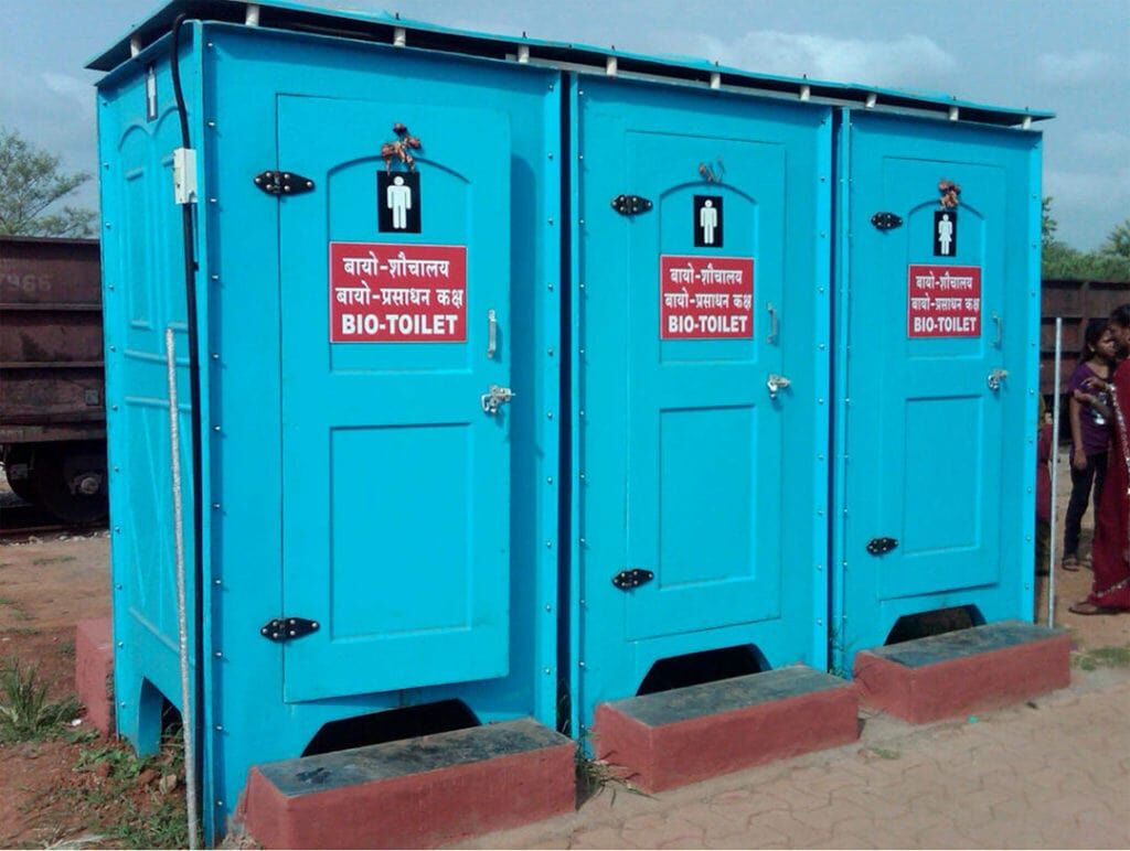 Why Bio Toilet is a Sustainable Sanitation Solution 1 Three blue portable bio-toilets with signs in Hindi and English ("BIO-TOILET"), likely for public use in India.