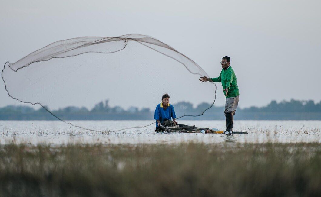 The Vital Role of Technology and Research in the Future of Fish Farming 1 Two people fishing with a net in shallow water, showcasing traditional methods in fish farming.